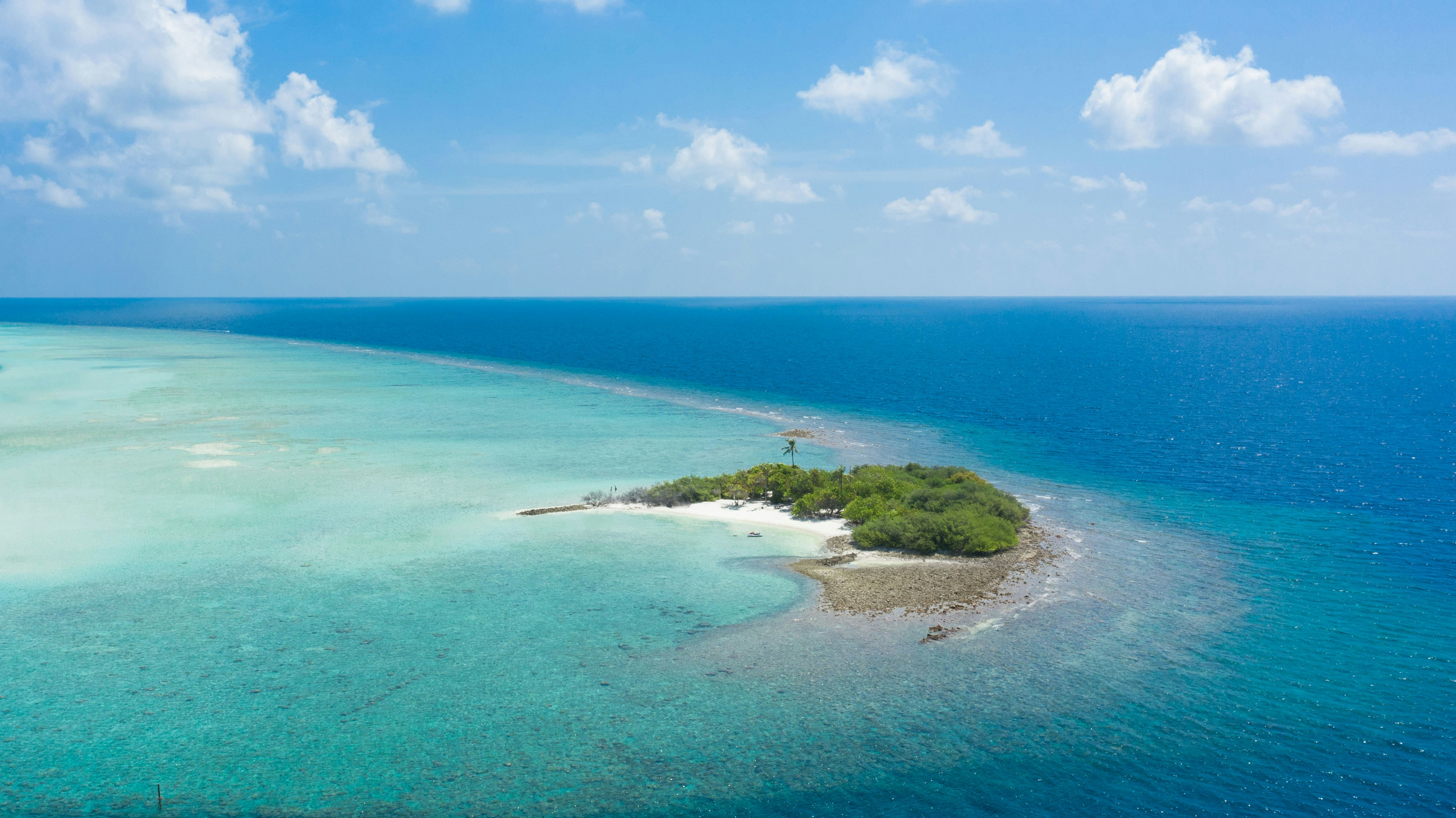 green island in the middle of blue sea under blue sky and white clouds during daytime